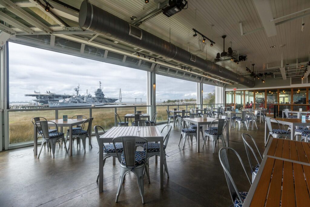 Looking back toward the bar and indoor dining room with a panoramic view of the Charleston Harbor and Yorktown Battleship from within the open air dining room at The Charleston Harbor Fish House.