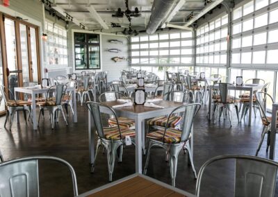 The Fish House indoor/outdoor dining room with rollup windows, metal tables, concrete floors and fish decor on the walls.